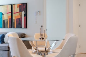 A modern dining area with a glass table, four chairs, and two candlesticks. - Urban Oasis Downtown | Pools Gym & Entertainment (Montreal)