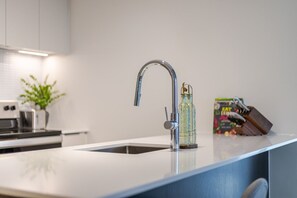 Una cocina moderna con un grifo de acero inoxidable, una botella de vidrio y una caja de barritas energéticas 'Fat Free' sobre la encimera.