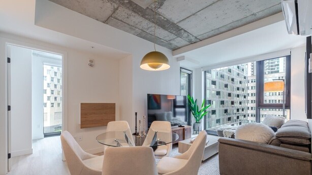 Uma sala de estar moderna com uma mesa de jantar de vidro, assentos confortáveis, uma televisão grande e vista para a cidade.
