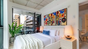 Quarto de hotel moderno com cama, abajures, varanda com vista e arte abstrata na parede.