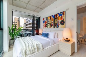 Ein modernes Hotelzimmer mit Bett, Nachttischlampen, einem Balkon mit Aussicht und abstrakter Kunst an der Wand.