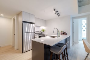 A modern kitchen with a stainless steel refrigerator, a built-in oven, and a sink with a faucet. There are two bar stools at the island. - Urban Oasis Downtown | Pools Gym & Entertainment (Montreal)