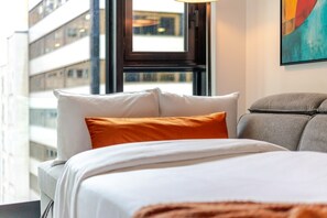 Ein Hotelzimmer mit Bett, Kissen, einem Fenster und einem Bild an der Wand.