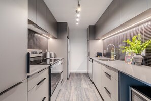 A modern kitchen with stainless steel appliances, a built-in oven, and a countertop with a potted plant. - Modern City Retreat | Balcony + Resort Amenities (Montreal)