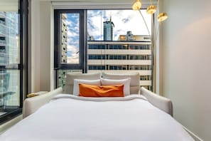 Ein modernes Hotelzimmer mit einem großen Bett, Blick auf die Stadt durch ein großes Fenster und einer stilvollen Pendelleuchte.