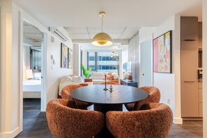 A modern dining area with a round table surrounded by textured chairs, a pendant light, and artwork on the walls. - Modern City Retreat | Balcony + Resort Amenities (Montreal)