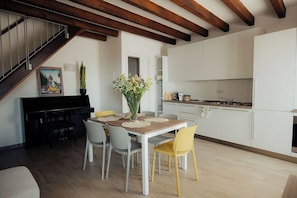 A dining area with a piano, a table with chairs, and a kitchen in the background. - With a breathtaking lake view, brand new apartment for families and couples (Cavaion Veronese)