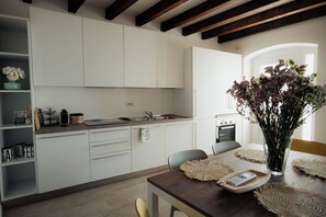 A modern kitchen with white cabinets, a dining table with placemats, and a vase with flowers. - With a breathtaking lake view, brand new apartment for families and couples (Cavaion Veronese)