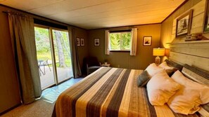 A hotel room with a bed, a chair, a window, and a door leading to a balcony.