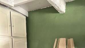 Una habitación con pared verde, un armario blanco, una silla de madera y una lámpara de pie blanca.