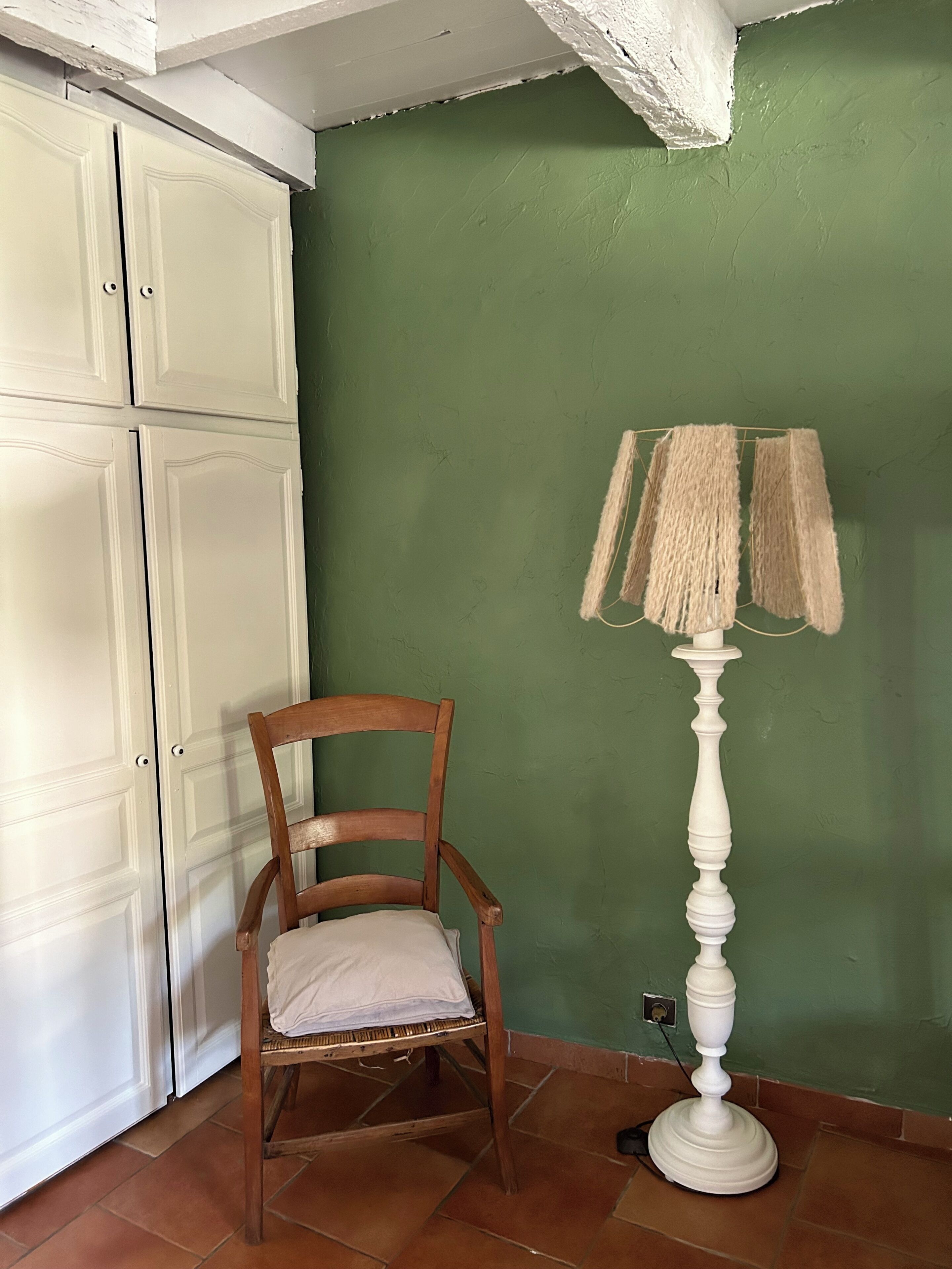 Een kamer met een groene wand, een witte garderobe, een houten stoel en een witte vloerlamp.