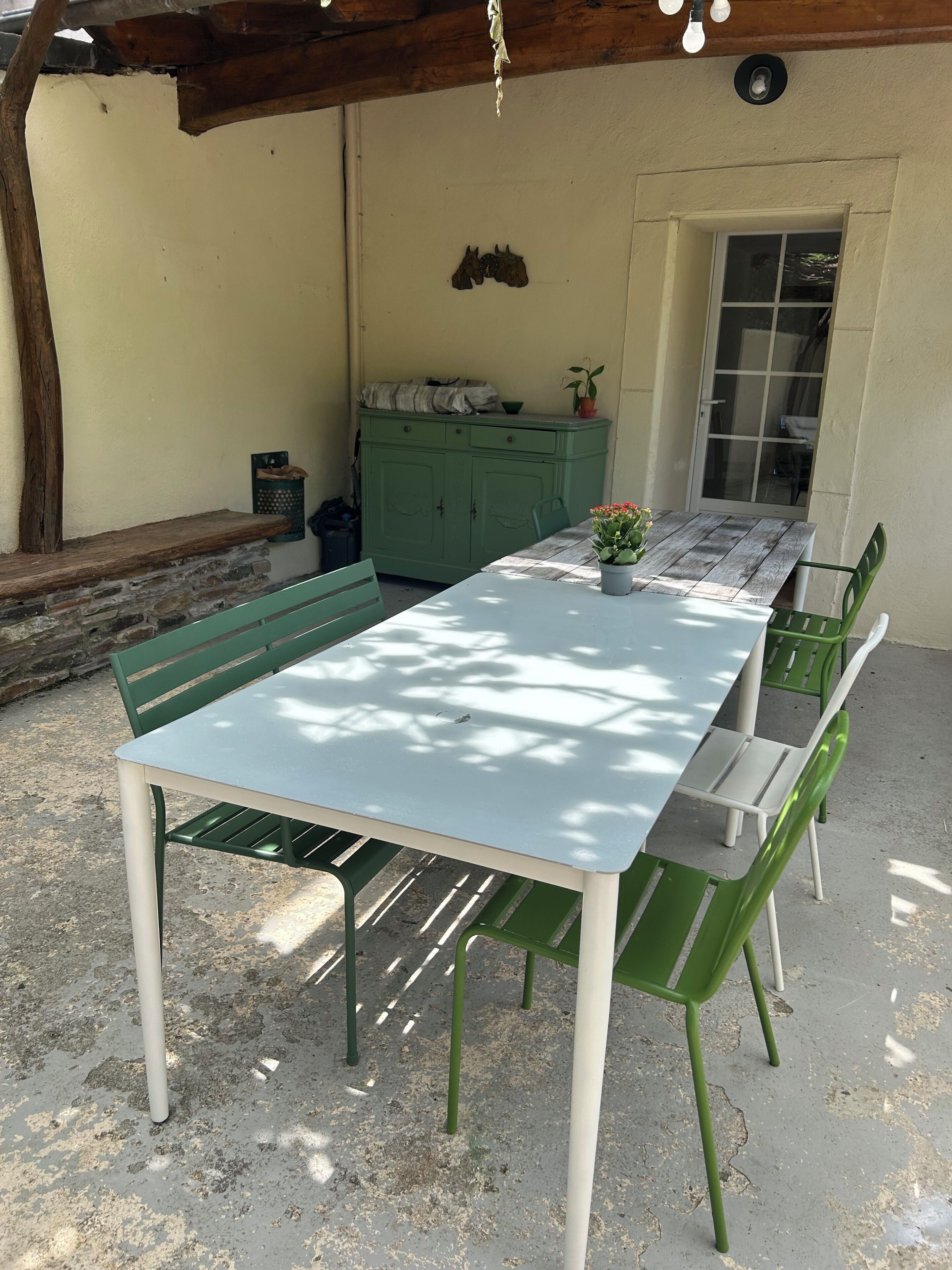 Een overdekt terras met een tafel, stoelen, een kast en een deur naar buiten.