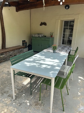 En overdækket terrasse med et bord, stole, et skab og en dør til et udendørs område.