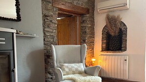 Una habitación con pared de piedra, chimenea, radiador y un sillón gris con una manta mullida.