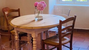 Una mesa de comedor con sillas, un jarrón con flores y una ventana con vistas a la vegetación.