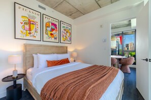 Ein Hotelzimmer mit Bett, Nachttisch, Fenster mit Blick auf die Stadt und drei Wandbildern im Picasso-Stil.