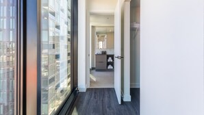Um interior moderno com uma janela ampla, uma área de cozinha com bancada e armários, e um corredor que leva a uma porta.