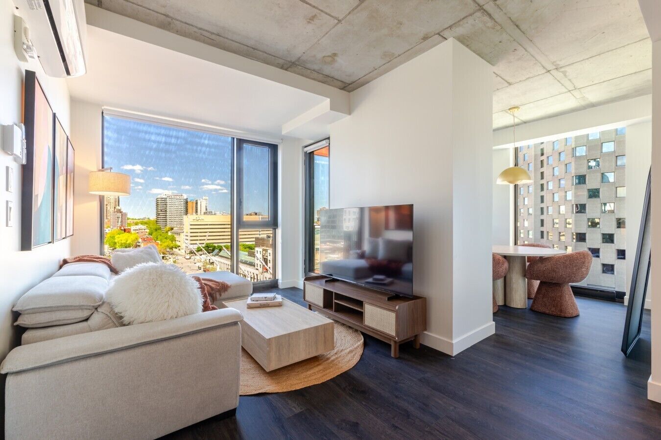 A modern living room with a large TV, a sofa, a coffee table, and a dining area with chairs.