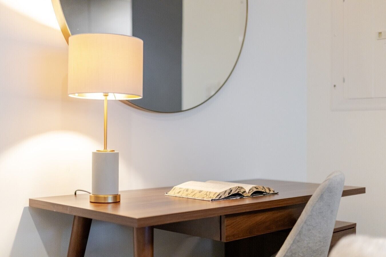 A wooden desk with a lamp, a mirror, and a book.