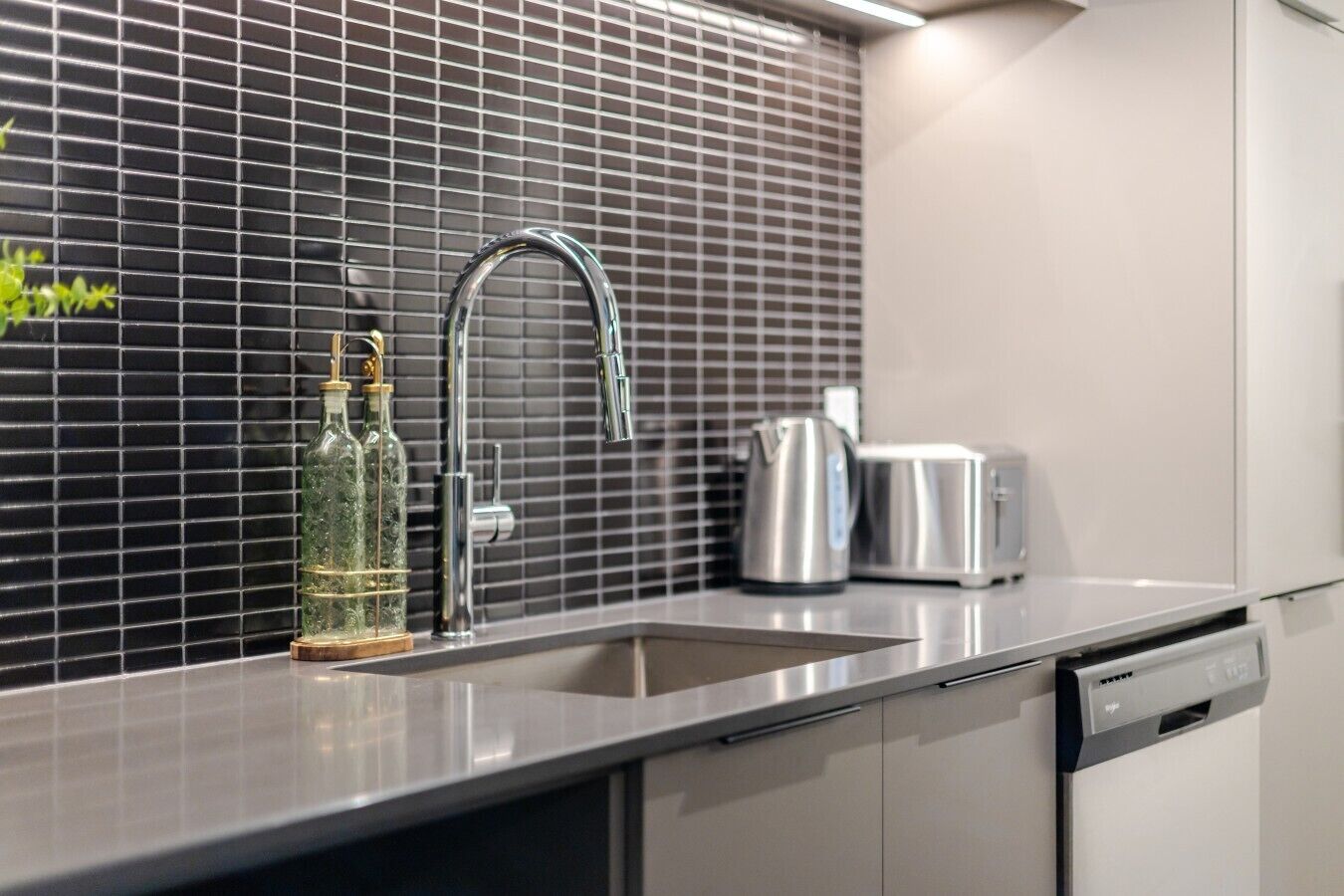 Una cocina moderna con un lavamanos de acero inoxidable, una tetera y un tostador sobre la encimera.