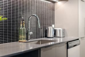 A modern kitchen with a stainless steel sink, a kettle, and a toaster on the counter. - Elegant Downtown Stay | Pools Gym & Rooftop (Montreal)