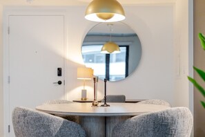 A round dining table with a modern lamp, a mirror, and a door in the background. - Elegant Downtown Stay | Pools Gym & Rooftop (Montreal)