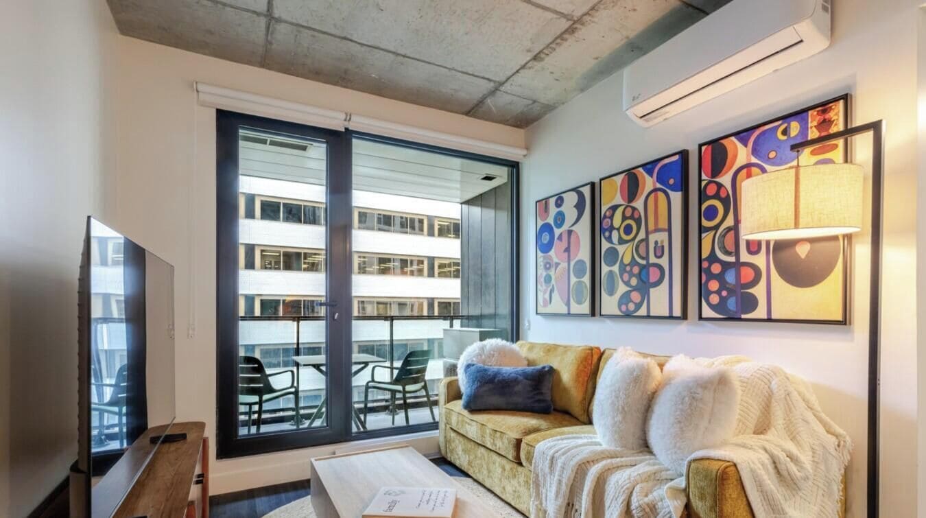 A living room with a sofa, a coffee table, a TV, and a large window with a view of a building.