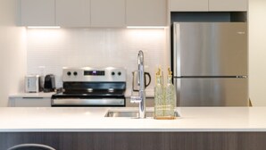 A modern kitchen with a stainless steel refrigerator, a built-in oven, and a white countertop. - City View Haven | Free Parking, Gym & Pool (Montréal)