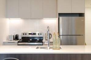 A modern kitchen with a stainless steel refrigerator, a built-in oven, and a white countertop. - City View Haven | Free Parking, Gym & Pool (Montréal)