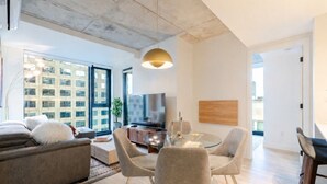 A modern living room with a sofa, TV, glass table, and chairs. - City View Haven | Free Parking, Gym & Pool (Montréal)