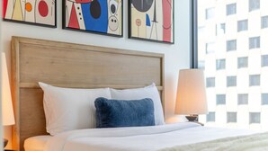 A hotel room with a bed, a nightstand with a lamp, and abstract art on the wall. - Urban Luxe Stay | Free Parking (Montréal)