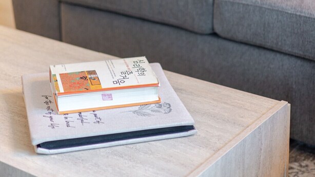 A modern living room with a grey sofa, a white fluffy pillow, and a wooden coffee table with a book. - Urban Luxe Stay | Free Parking (Montréal)