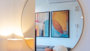 A round mirror reflecting a room with a blue sofa, colorful abstract paintings, a globe, and a lamp on a wooden table. - Urban Luxe Stay | Free Parking (Montréal)