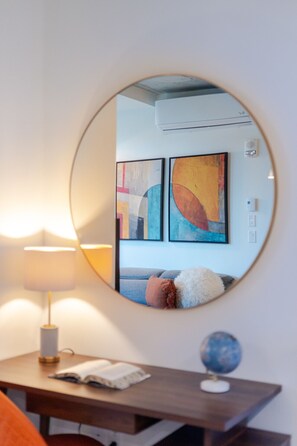 Ein runder Spiegel, der einen Raum mit einem blauen Sofa, farbenfrohen abstrakten Bildern, einem Globus und einer Lampe auf einem Holztisch reflektiert.