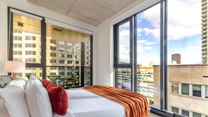 A modern hotel room with a large bed, a balcony, and a city view. - Urban Luxe Stay | Free Parking (Montréal)