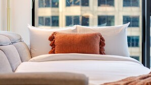 Habitación de hotel con cama, almohadas, una lámpara y vista a un edificio a través de la ventana.