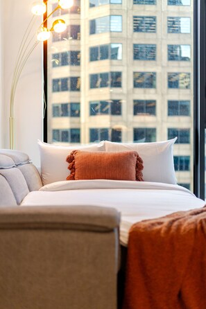 Ein Hotelzimmer mit Bett, Kissen, einer Lampe und Blick auf ein Gebäude durch das Fenster.