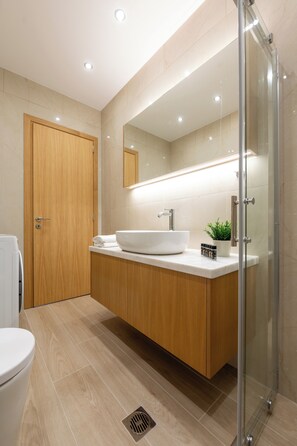 A modern bathroom with a wooden vanity, a white sink, a mirror, and a glass shower enclosure. - Maris Apts Kato Gouves (Kato Gouves)
