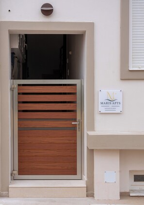 Entrada de un edificio con una puerta de madera, un letrero con 'MARIS APTS' y un logotipo, y una pequeña ventana a la derecha.