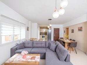 A modern living room with a grey sectional sofa, a wooden coffee table with a floral table runner, and a dining area with a wooden table and chairs. - Maris Apts Kato Gouves (Kato Gouves)