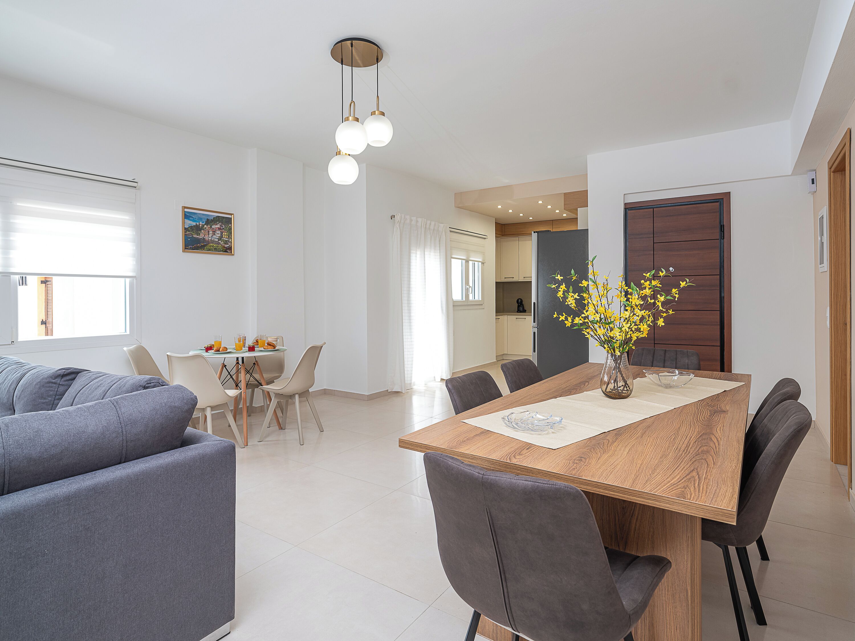 A modern dining area with a wooden table, grey chairs, and a vase with yellow flowers.