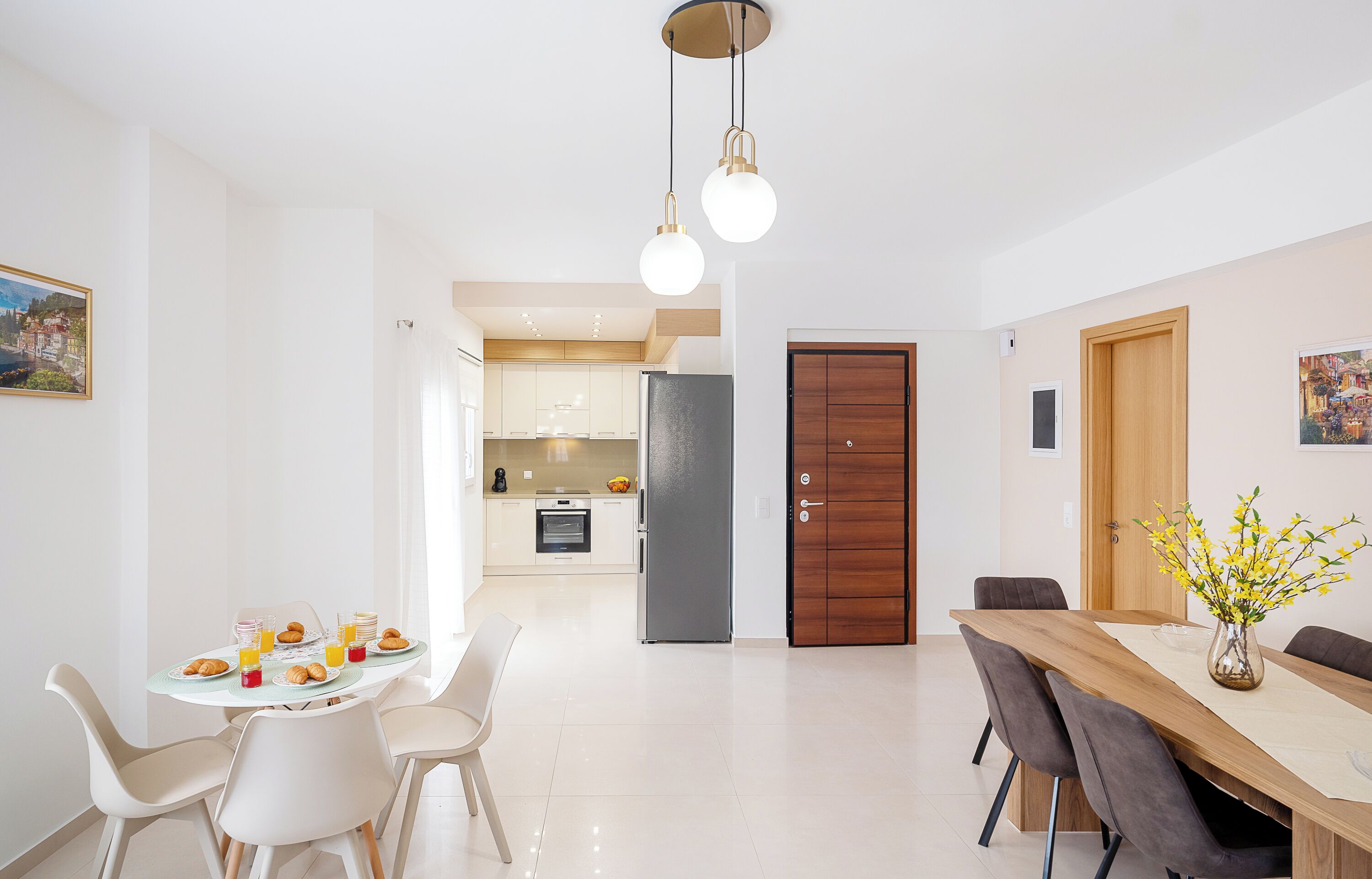 Ein moderner Essbereich mit einem für das Frühstück gedecktem Tisch, einer Küche im Hintergrund und einer Holztür.