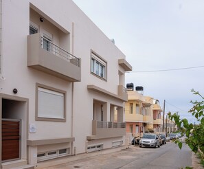 Rua residencial com edifícios modernos, portão fechado e carros estacionados.