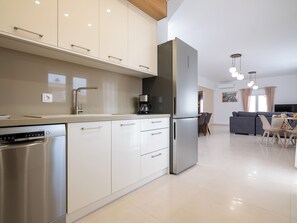 Una cocina moderna con electrodomésticos de acero inoxidable, una zona de comedor con sofá y sillones, y un televisor de pantalla plana.