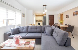 Una sala de estar moderna con un sofá seccional gris, una mesa de centro de madera con una revista y un jarrón de flores.