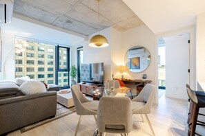 A modern living room with a sofa, TV, dining table, and chairs. - Downtown Prestige | Free Parking (Montréal)