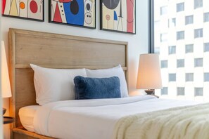 Ein Hotelzimmer mit einem Bett, einem Nachttisch mit Lampe und abstrakter Kunst an der Wand.