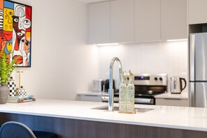 Eine moderne Küche mit weißer Arbeitsplatte, Edelstahlgeräten und einem farbenfrohen abstrakten Gemälde an der Wand.