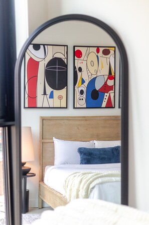 A bedroom with a wooden headboard, a bed with white and blue bedding, and two abstract paintings on the wall. - Skyline Retreat | Free Parking & Pool (Montréal)