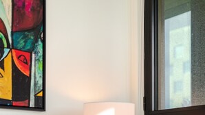 A bed with a red pillow, a lamp on a small table, and a painting on the wall. - Skyline Retreat | Free Parking & Pool (Montréal)